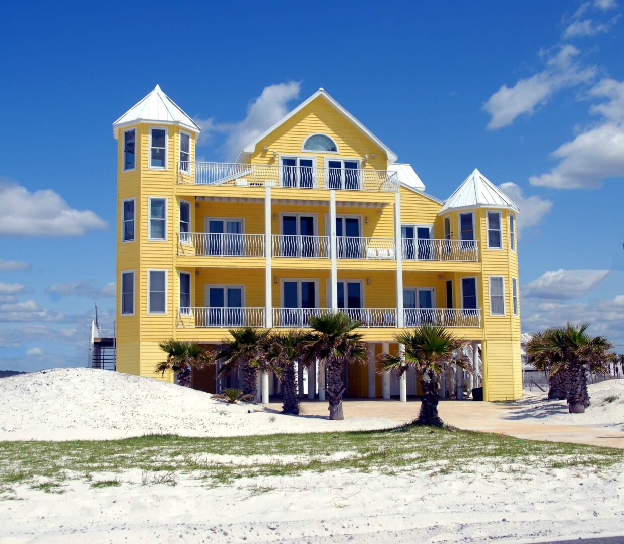 A yellow house on the beach with palm trees.