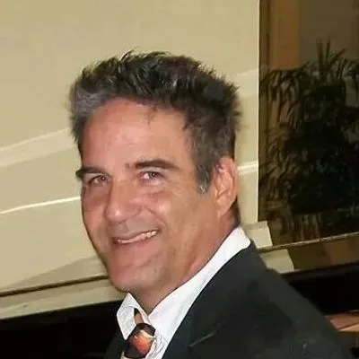 A man in a suit and tie smiles in front of a piano.